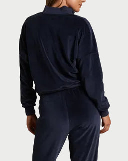 Person wearing a navy tracksuit standing against a plain wall.