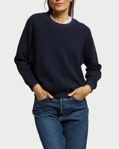 A person wears the perfectwhitetee Ziggy Sweatshirt in navy over a white shirt with blue jeans, hands in their pockets, standing against a plain light background with their face partially out of frame.