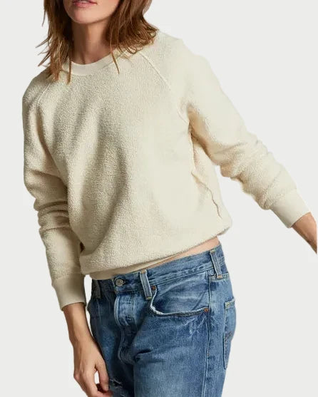 Woman wearing a cream sweater and blue jeans against a plain background