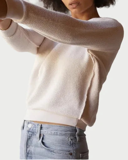 Woman wearing a beige sweater and blue jeans against a plain background