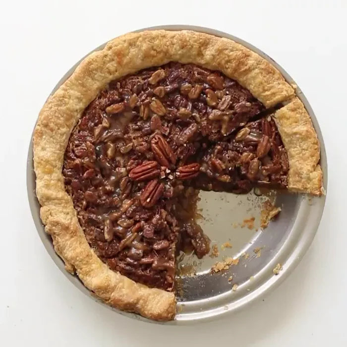 Pecan pie with two slices removed, showing pecan nuts on top and a golden crust in a metal pie pan.