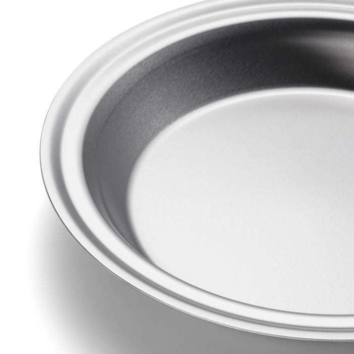 Round metal pie pan with rolled rim and light-gray nonstick interior, close-up, angled view