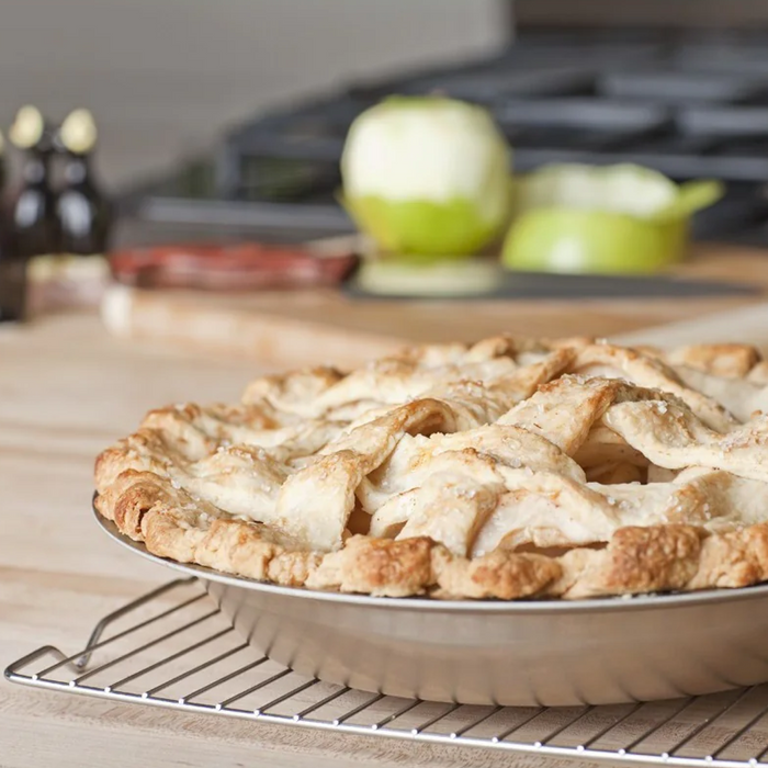 Front view of stainless steel pie pan with baked double-crust apple pie, showing rolled rim and smooth interior on wire rack