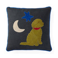 A square dark gray throw pillow with a blue piped edge, featuring an embroidered design of a golden dog wearing a red collar, a blue star, and a cream crescent moon.
