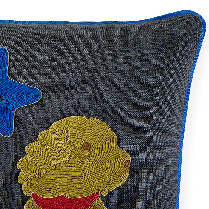 Close-up of a dark gray textured throw pillow with a blue piped edge, featuring an embroidered yellow dog with a red collar and a blue star on the left.