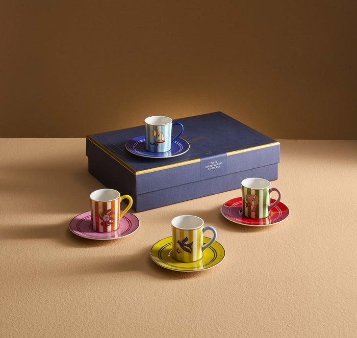 Set of colorful coffee cups and saucers with a decorative box on a beige surface.