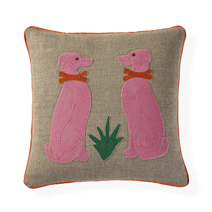 A square beige linen throw pillow with orange piping, featuring an embroidered design of two pink dogs wearing orange collars and a green plant in the center.