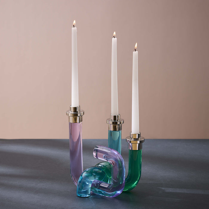 Three candle holders with colorful glass bases on a gray surface.