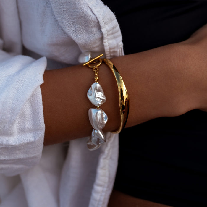 Gold and pearl bracelets on a wrist with a white sleeve