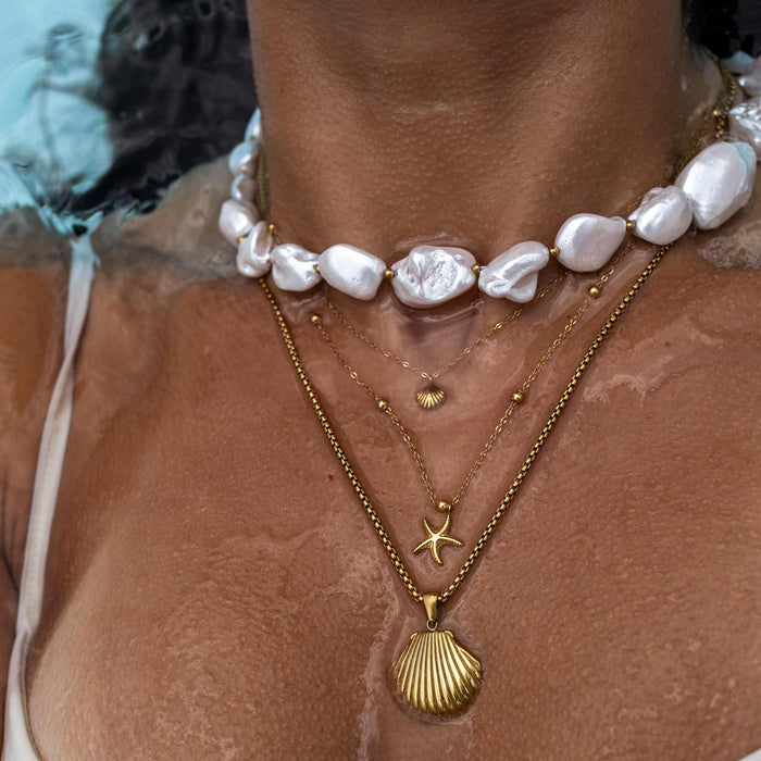 A close up of a neck under water wearing a necklace stack with three necklaces featuring large white baroque pearls and shell pendants