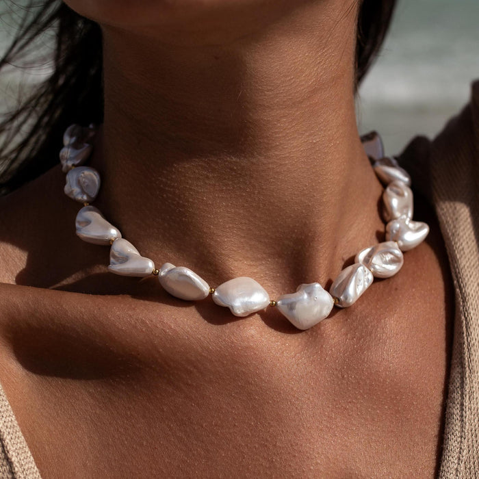 a chunky white baroque pearl necklace with small gold beads
