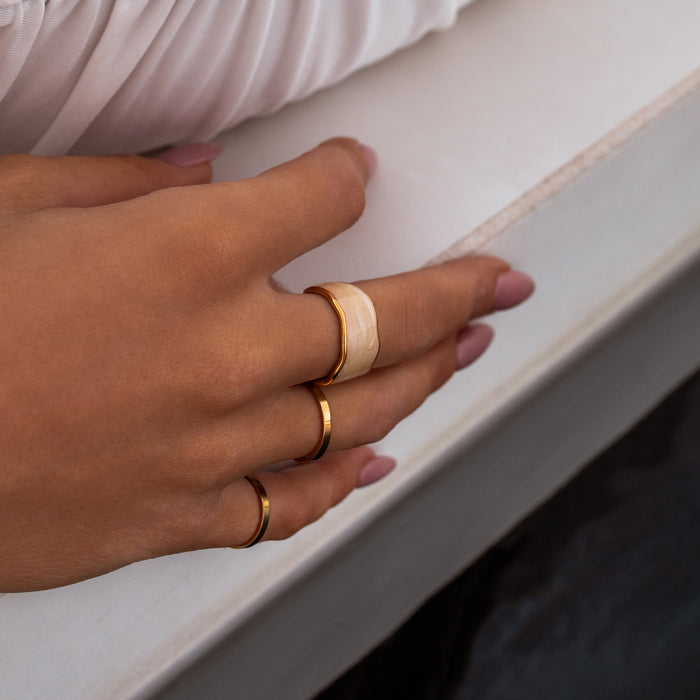 Close up of a hand on the edge of a pool wearing three water resistant rings including two simple gold bands and one iridescent gold ring with a pearl like center