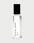 A Riddle Oil - Nude Beach 8ml bottle, made of clear glass and sealed with a black cap, contains a transparent liquid. The label features the words "nude beach" in lowercase letters. The design is minimalist and sleek, showcasing the trending Nude Beach scent by Riddle Oil.
