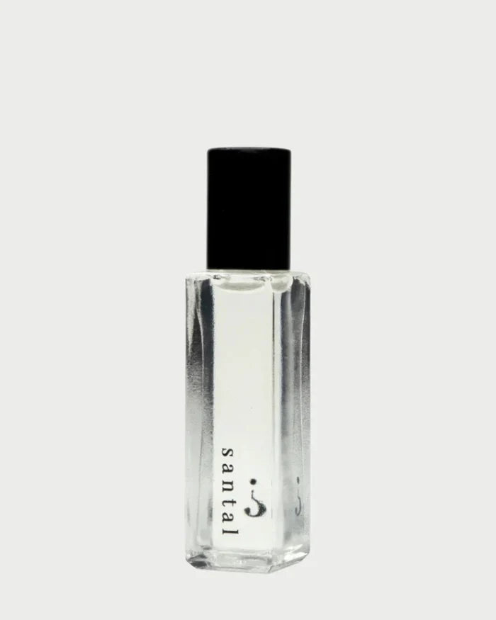 A clear rectangular bottle with a black cap from Riddle Oil exudes an exquisite fragrance. The label on this 8ml "Riddle Oil: Santal" perfume features a minimalist design on the lower part of the bottle, showcasing its sandalwood-infused santal scent against a pale gray background.
