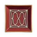 A square ceramic dish with a deep burgundy red interior, featuring a cream-colored geometric trellis pattern in the center and a thin gold rim, shown against a plain white background.