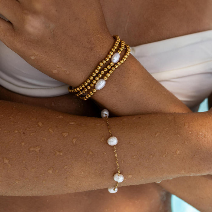 a gold and pearl wrist stack featuring bracelets with dainty gold beads, delicate gold chains and freshwater pearls