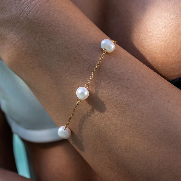 A gold-plated bracelet with a delicate chain and freshwater pearls on a person's wrist.