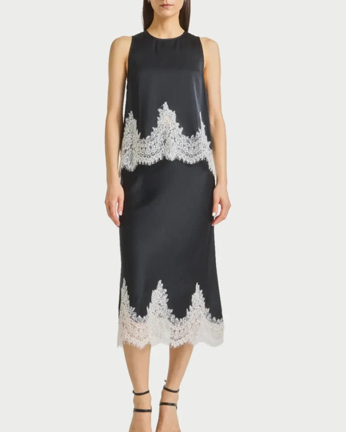 Black top and skirt with white lace details worn by a model on a gray background