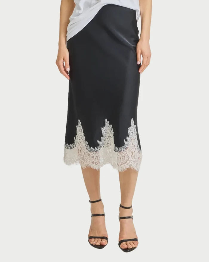Woman wearing a white top and black skirt with lace details on a gray background