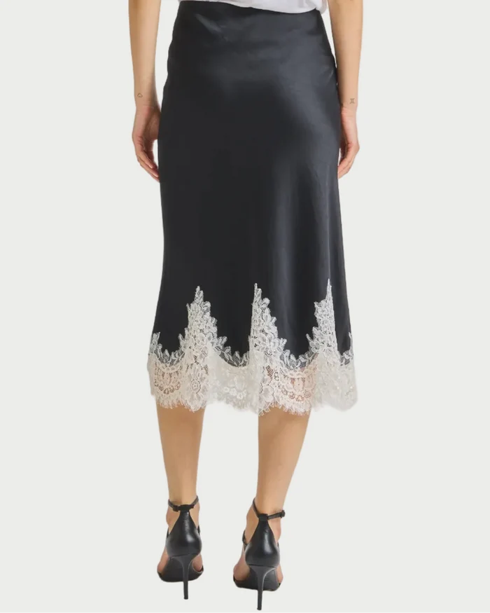 Person wearing a black skirt with lace trim and a white top on a light gray background