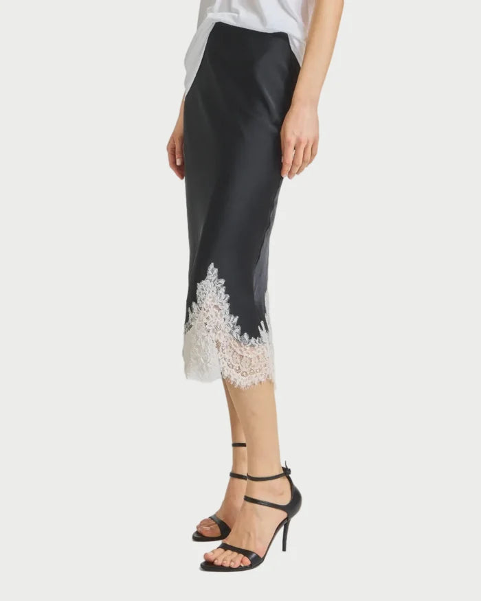Woman wearing a white top and black skirt with lace details on a plain background