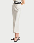 Woman wearing a white sleeveless top and high-waisted white pants with a black belt on a white background