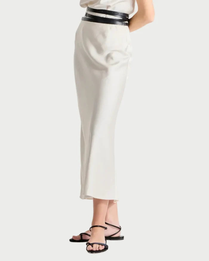 Woman wearing a white sleeveless top and high-waisted white pants with a black belt on a white background