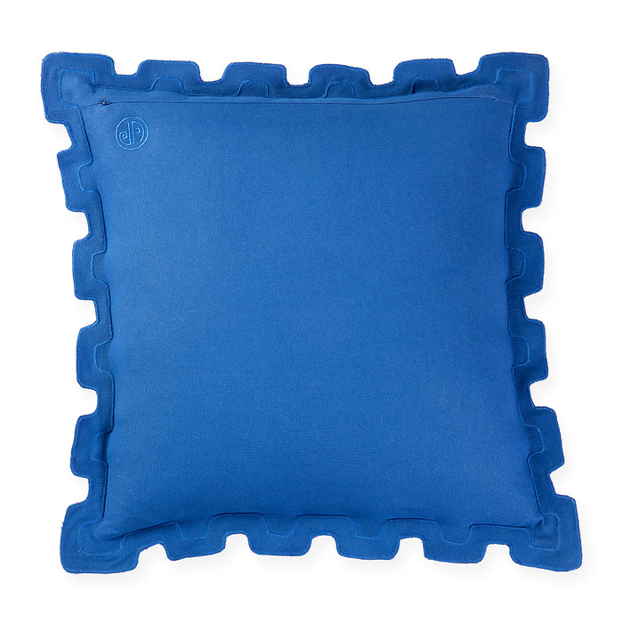 A square royal blue throw pillow with a decorative scalloped or wavy piped border, shown against a plain white background. A small circular monogram logo is embroidered in the top-left corner.