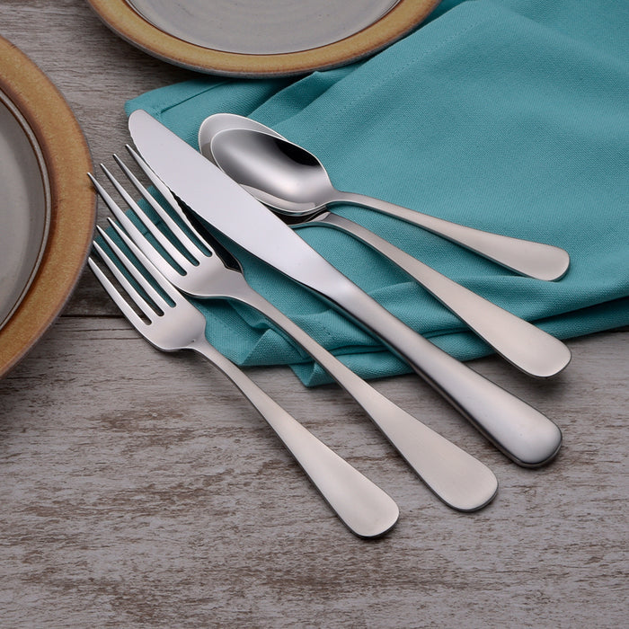Angled view of Satin Annapolis 45-piece stainless flatware showcasing satin finish on forks, knife, and spoons on teal napkin and wood table