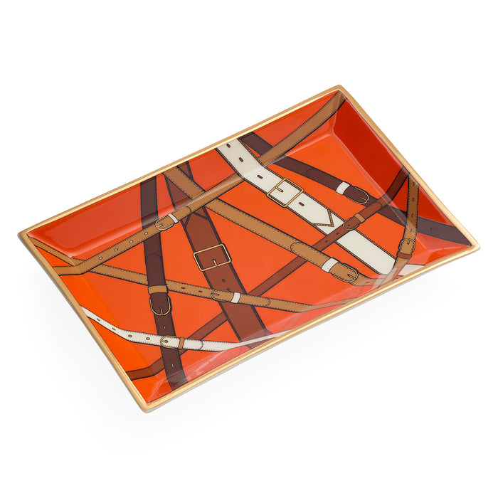 A rectangular ceramic tray with a glossy orange background and a printed pattern of overlapping leather straps in brown, tan, and cream, finished with a gold-toned rim.