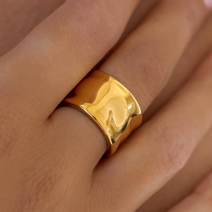 A gold melted wide band ring on a person's finger, showcasing its shiny surface.