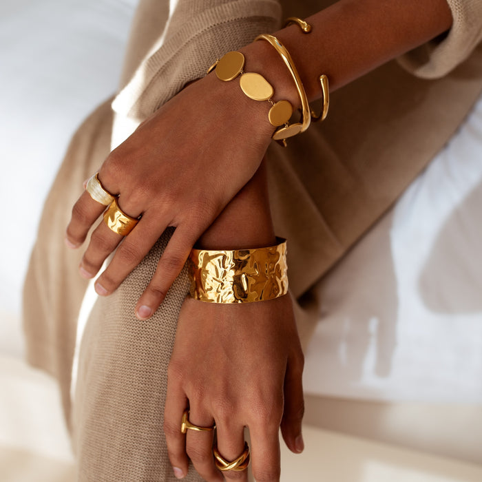 Close-up of hands wearing unique gold bracelets and rings on a neutral background