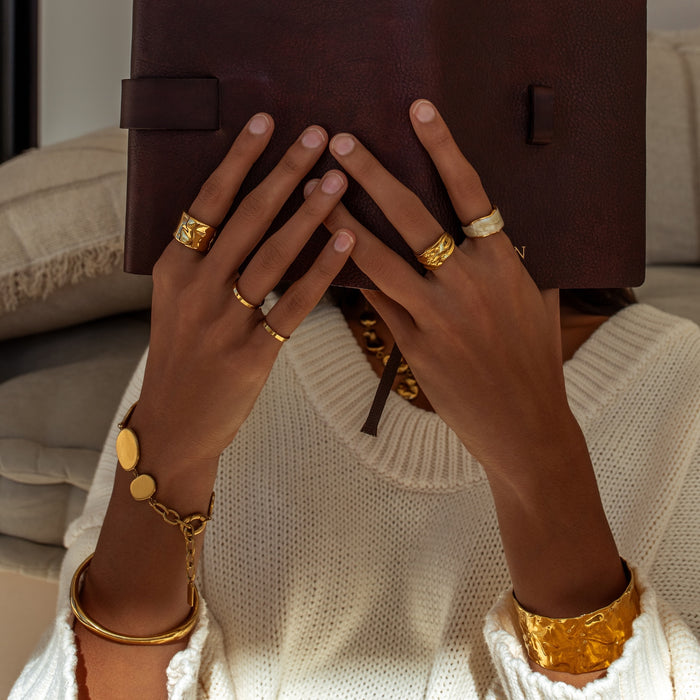 Close-up of hands wearing gold rings and bracelets, holding a brown leather book.
