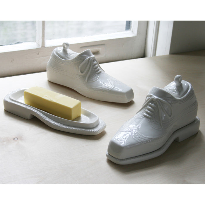 White ceramic shoes and a bar of soap on a light wooden surface with a window in the background.