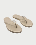 The Solei Sea Indie Flip Flop by Solei Sea features metallic gold vegan leather, thin straps, a cushioned footbed, and a simple design, shown against a white background.