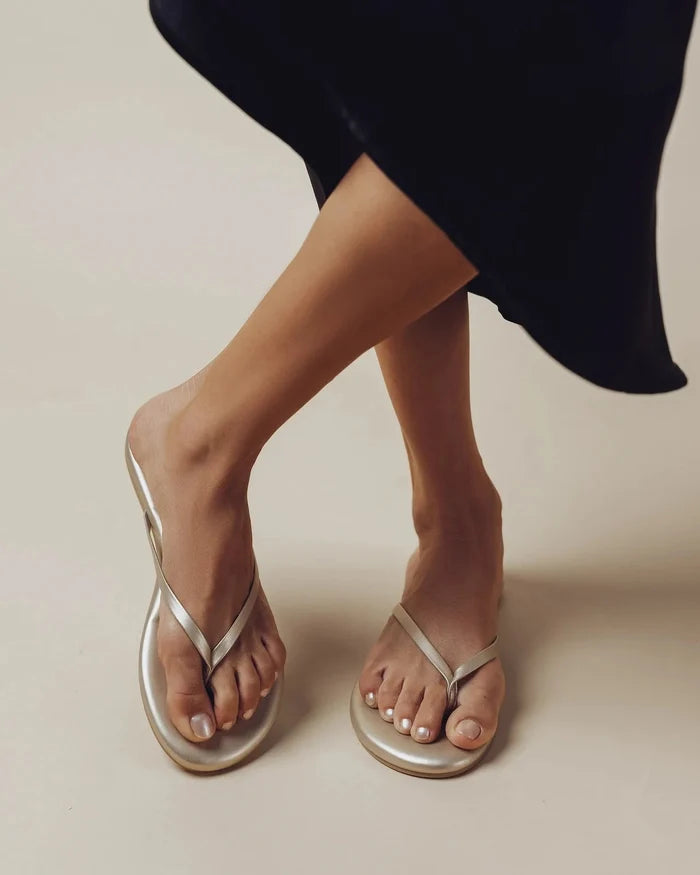 Silver flip-flops worn with a black skirt on a neutral background