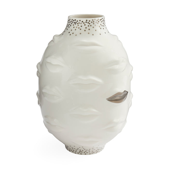 A white ceramic vase sculpted with a stylized face, featuring textured lips, closed eyes, and a metallic silver leaf detail on one eye. The neck and base are decorated with small metallic gold dots, set against a plain white background.