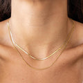 A close-up image of a person wearing a dainty double-layer gold herringbone necklace.