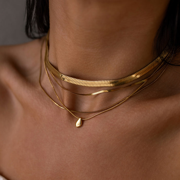 Close-up of a person wearing multiple gold necklaces on a neutral background