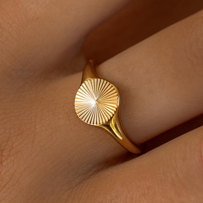 An 18K gold-plated stainless steel ring with a sunburst design on the top, worn on a person's finger.