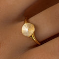 An 18K gold-plated stainless steel ring with a sunburst design on the top, worn on a person's finger.