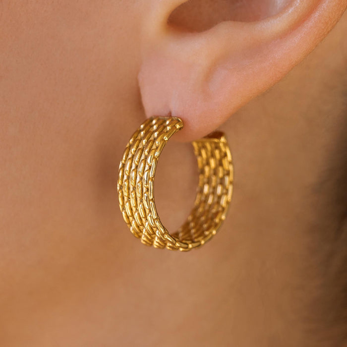 A close-up image of a woman's ear wearing a gold beaded texture hoop earring.