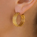 A close-up image of a woman's ear wearing a gold beaded texture hoop earring.