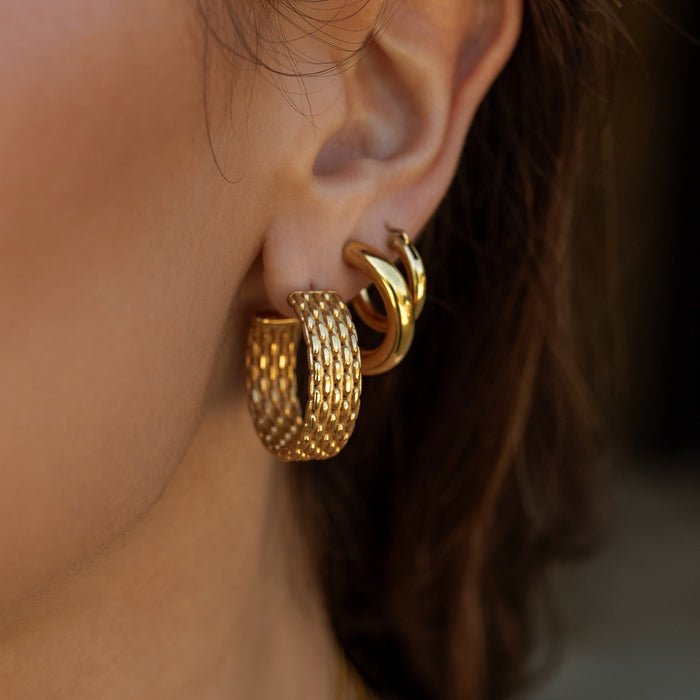 Close-up of a person wearing gold hoop earrings with a blurred background