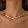 A close-up image of a person wearing a thick gold herringbone necklace.