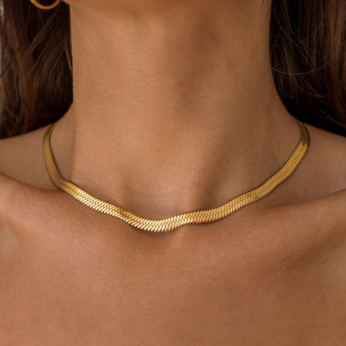 A close-up image of a person wearing a thick gold herringbone necklace.