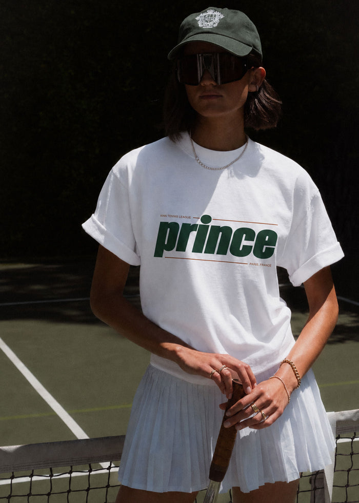 a woman on a tennis court wearing a Kinn x Prince Tennis League Tee and a Club Cap