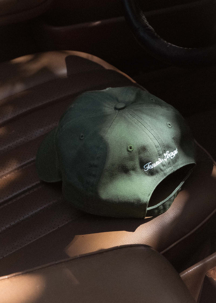 The Kinn x Prince The Club Cap sitting on a car seat showing the back with "Tennis League" embroidered on it