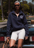 woman leaning on a vintage car wearing a Kinn x Prince The Club Quarter-Zip Sweatshirt with white biker shorts and a headband