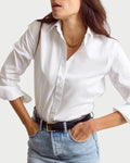 Woman wearing a white shirt and blue jeans with a gold necklace on a plain background